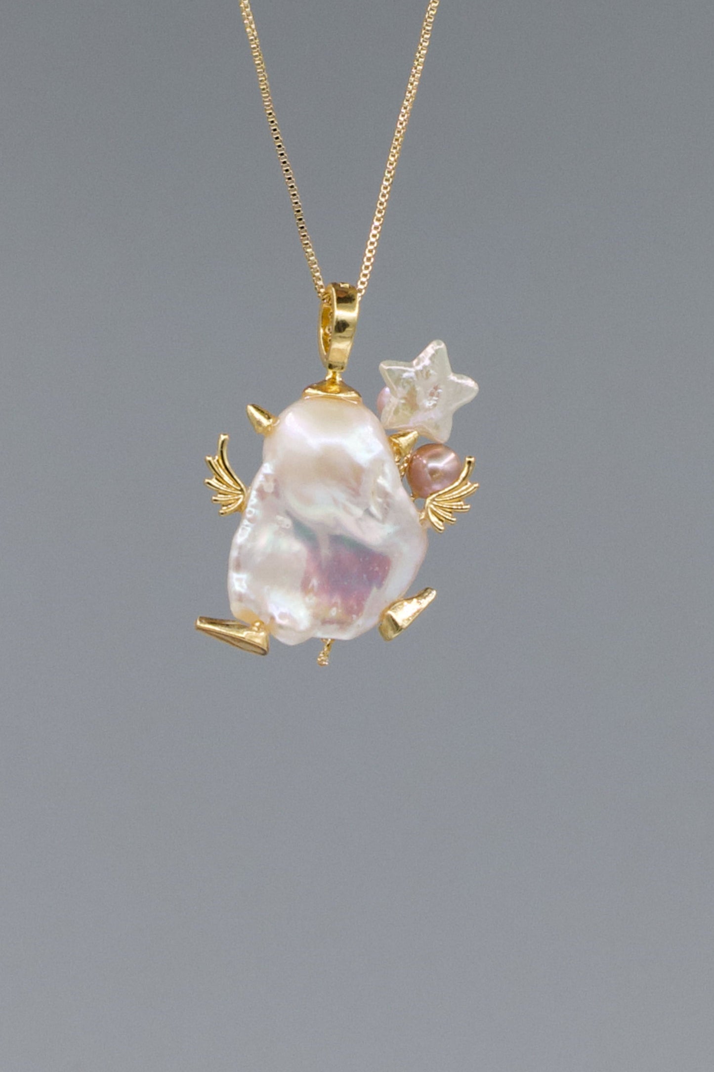 Gold pendant with a large baroque pearl and smaller stones on a gray background