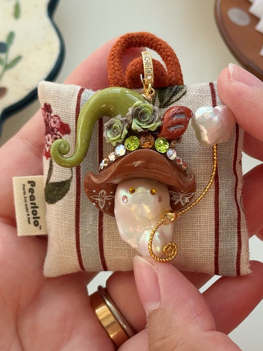 [PIECE10] Bakery Sprite baroque pearl necklace with taupe bagel-inspired hat, sculpted bagel detail, floral accents, gold wand, and natural baroque pearl