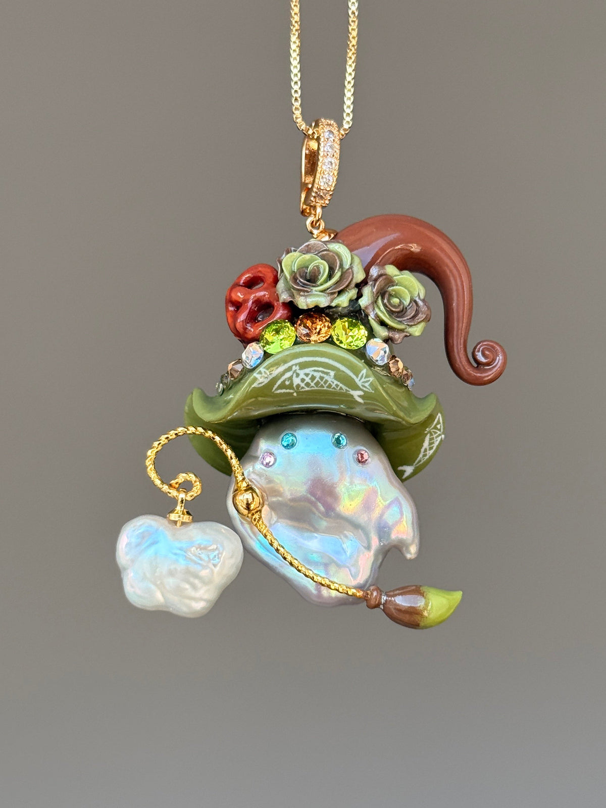 [PIECE07] Bakery Sprite baroque pearl necklace with olive green pretzel-inspired hat, sculpted pretzel detail, floral accents, gold wand, and natural baroque pearl