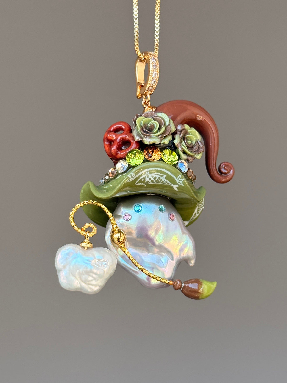 [PIECE07] Bakery Sprite baroque pearl necklace with olive green pretzel-inspired hat, sculpted pretzel detail, floral accents, gold wand, and natural baroque pearl